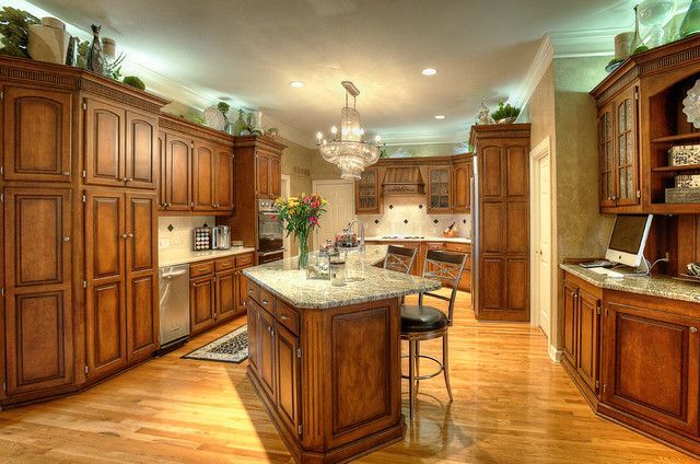 Spacious kitchen with wooden cabinets, marble island, chandelier, and warm hardwood floors