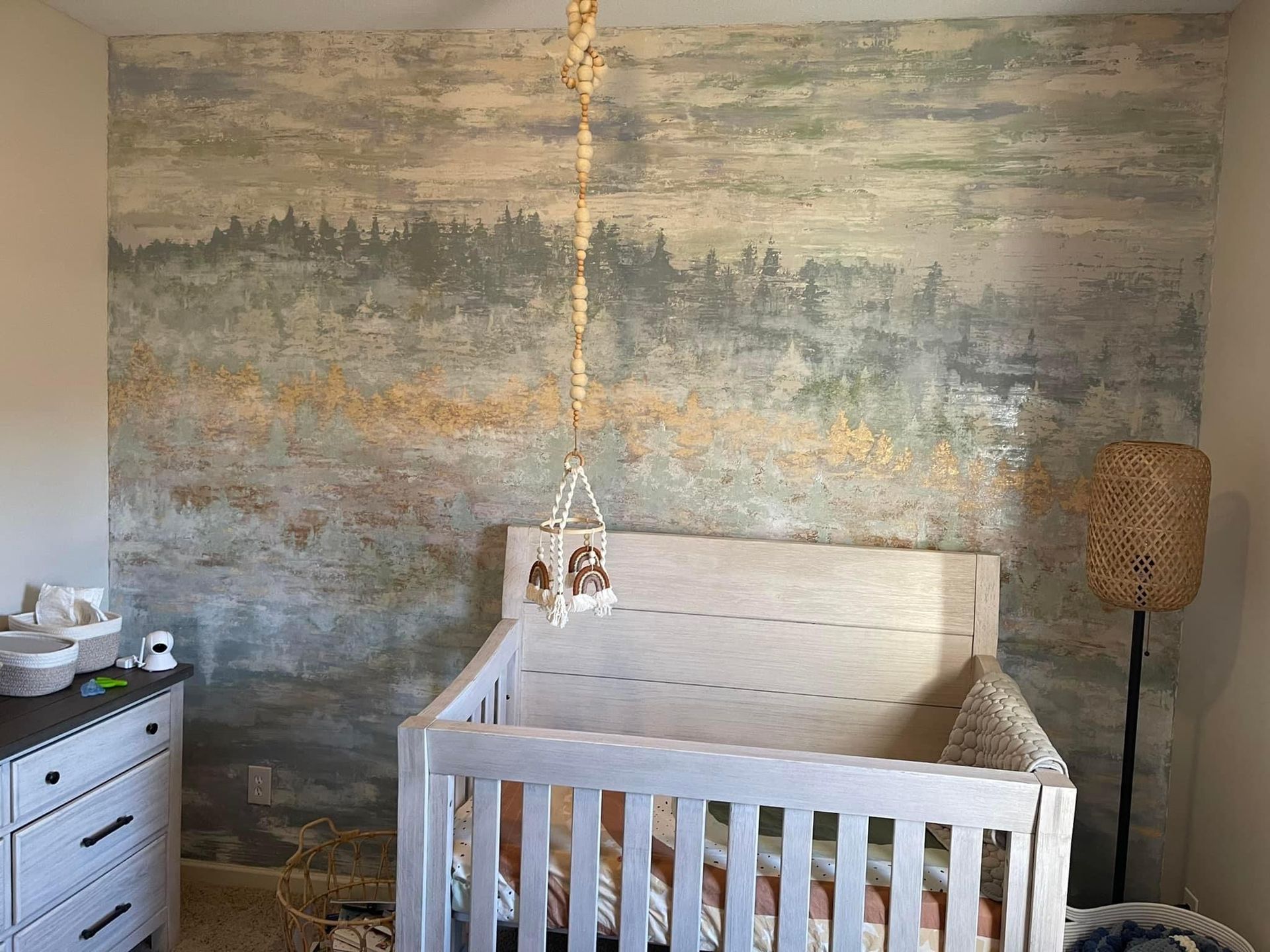 Nursery with white crib, forest mural wall, hanging light, and woven floor lamp