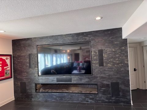 Living room with a wall-mounted TV, black stone accent wall, and electric fireplace below