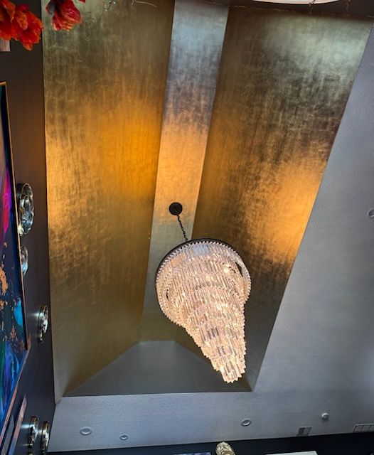Crystal chandelier hanging from a ceiling with gold panels and warm lighting.