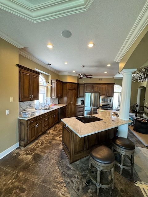 Spacious kitchen with dark wood cabinets, granite island, stainless appliances, and two stools under tray ceiling lights