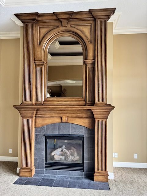 Wooden fireplace mantel with arched mirror above a lit firebox in a beige living room
