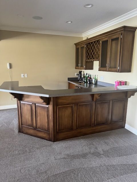 Empty home bar with dark wood cabinets and gray countertop in a carpeted room.