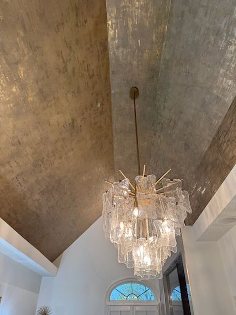 Chandelier hanging from a gold-toned vaulted ceiling above an arched window in a white room