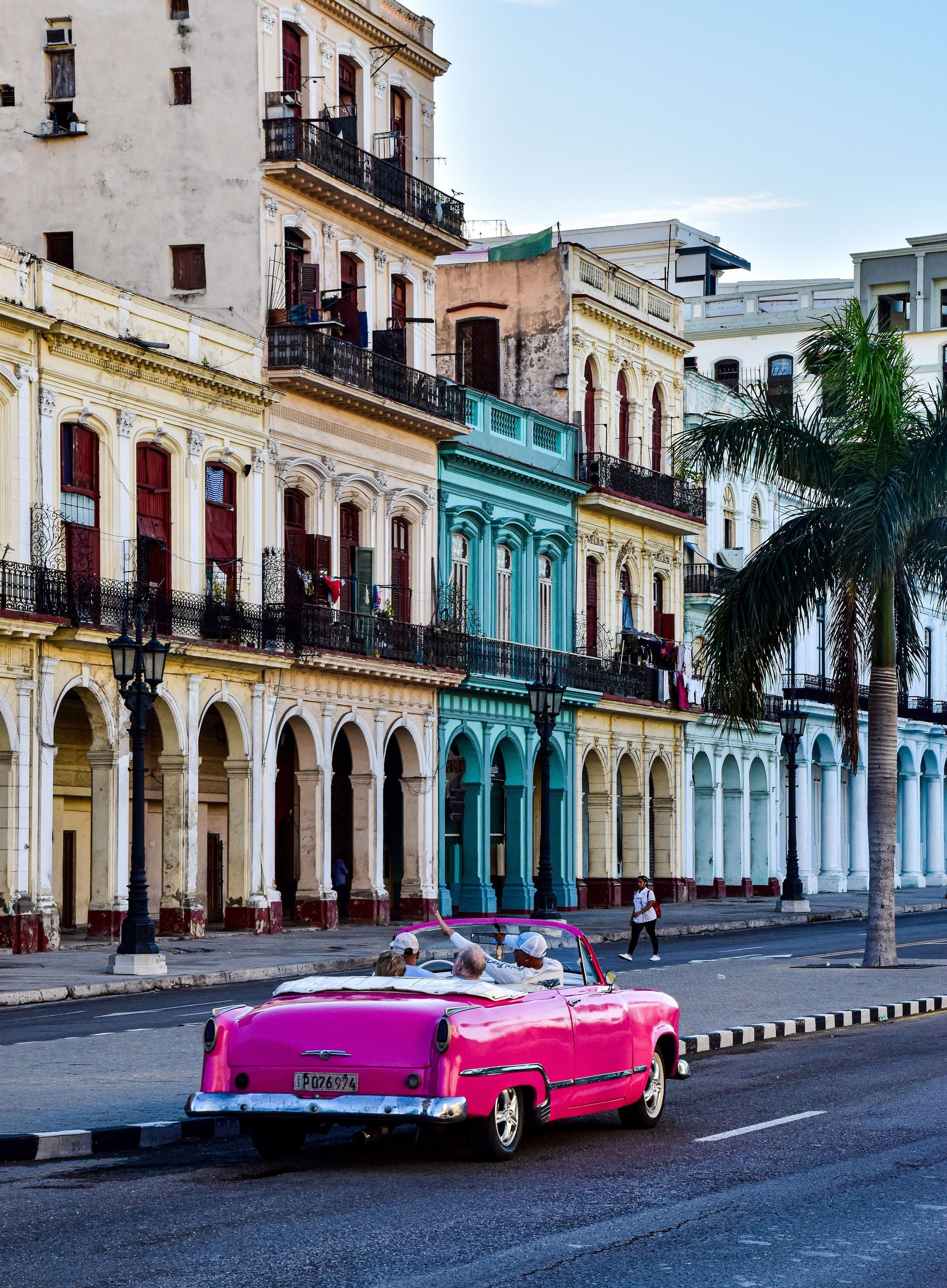 Un coche clásico de color rosa brillante en una calle flanqueada por coloridos edificios coloniales y palmeras.