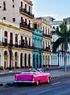 Un coche clásico de color rosa brillante en una calle flanqueada por coloridos edificios coloniales y palmeras.
