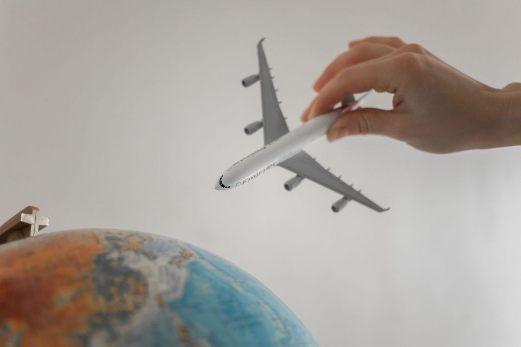Una mano sosteniendo un avión de juguete sobre un globo terráqueo con fondo liso.
