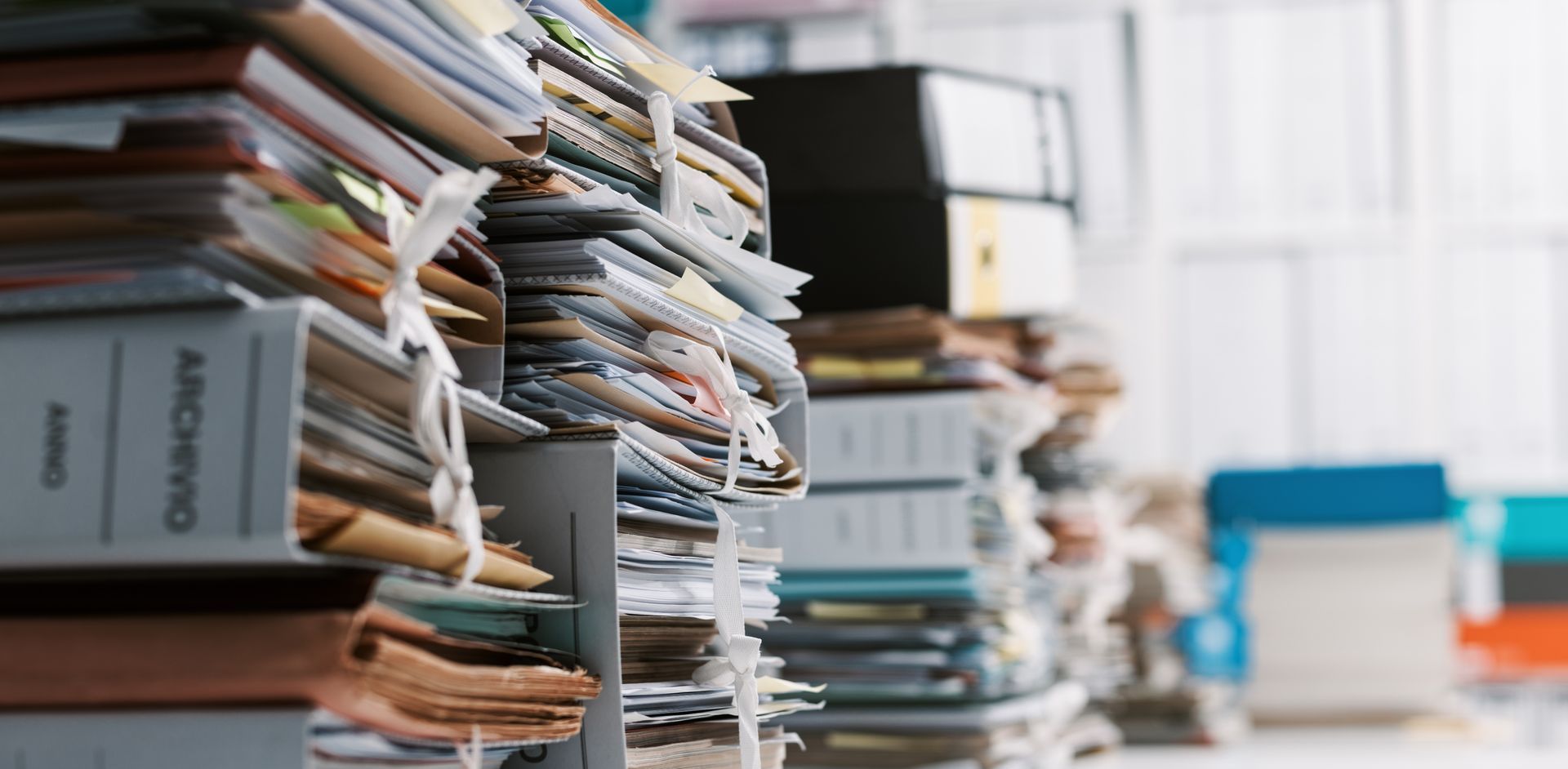 Stacks of papers and folders piled on office shelves and tables in a cluttered workspace