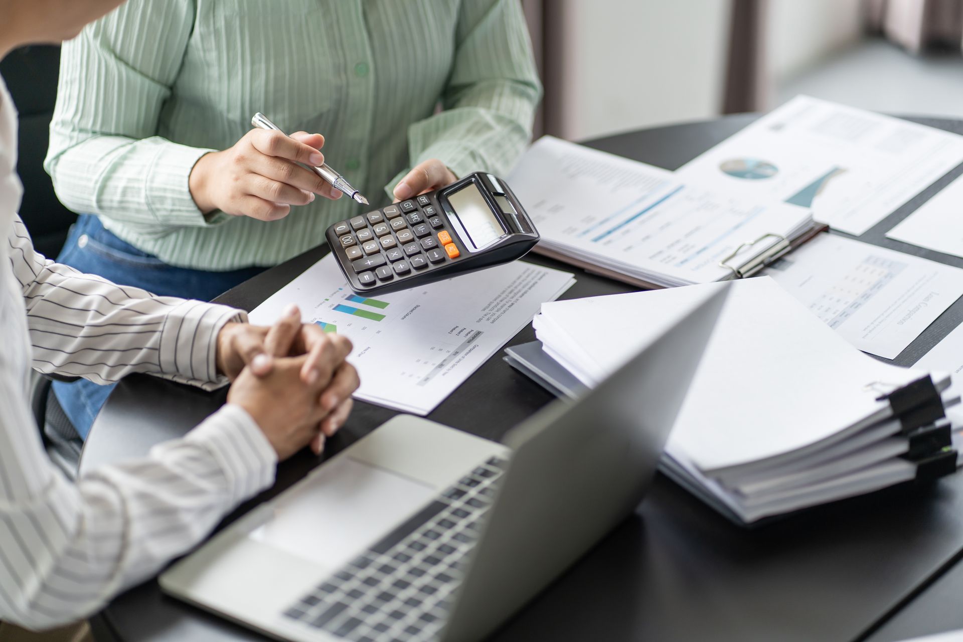 People reviewing financial documents at a desk with a laptop, calculator, and papers