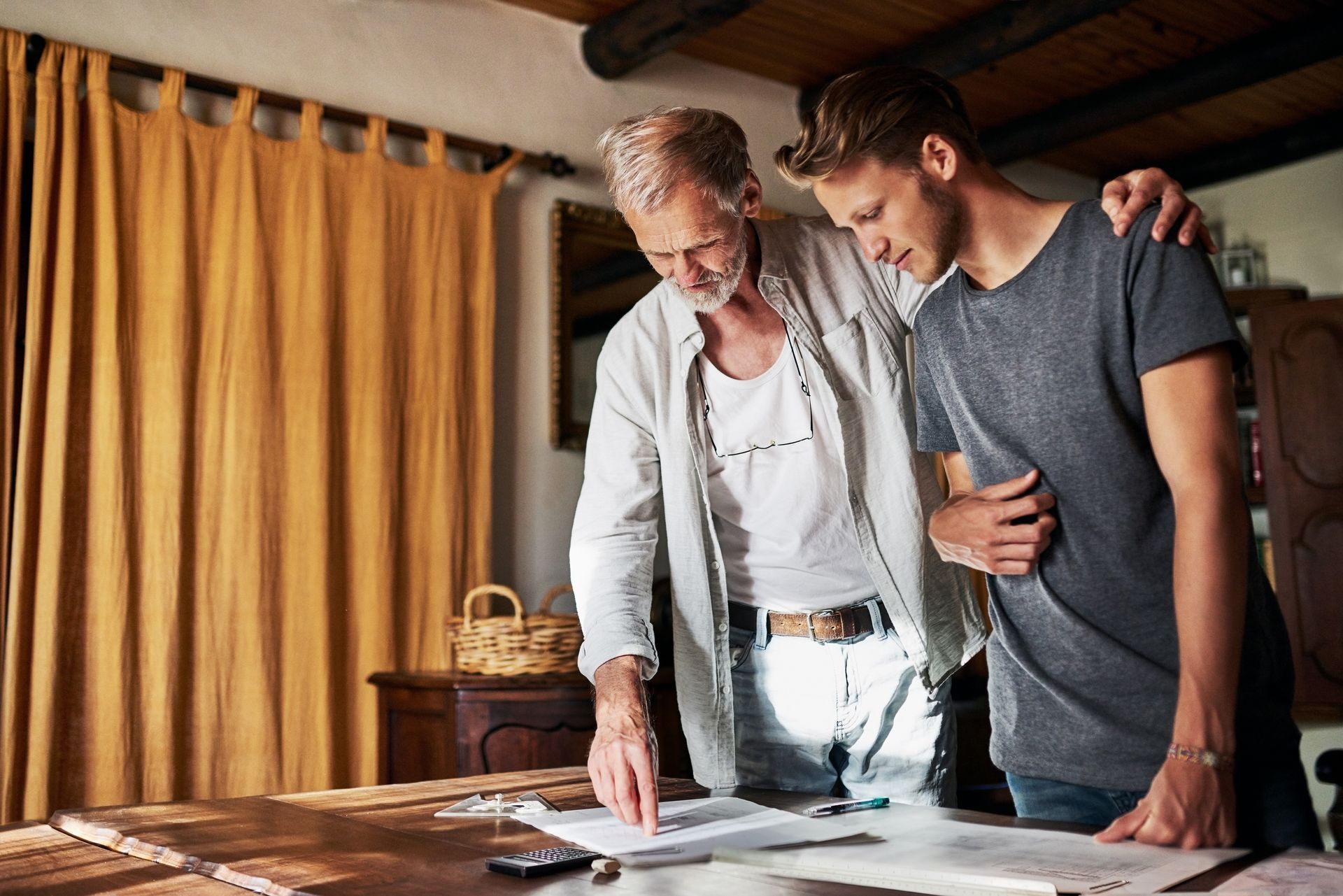 Two people reviewing plans on a table in a warmly lit room with yellow curtains