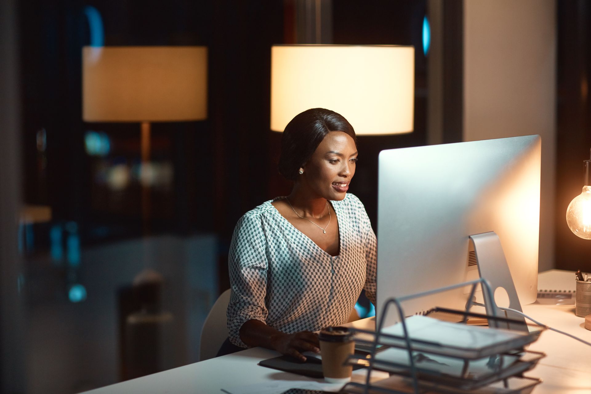 Woman working at a desk with a desktop computer in a softly lit office at night