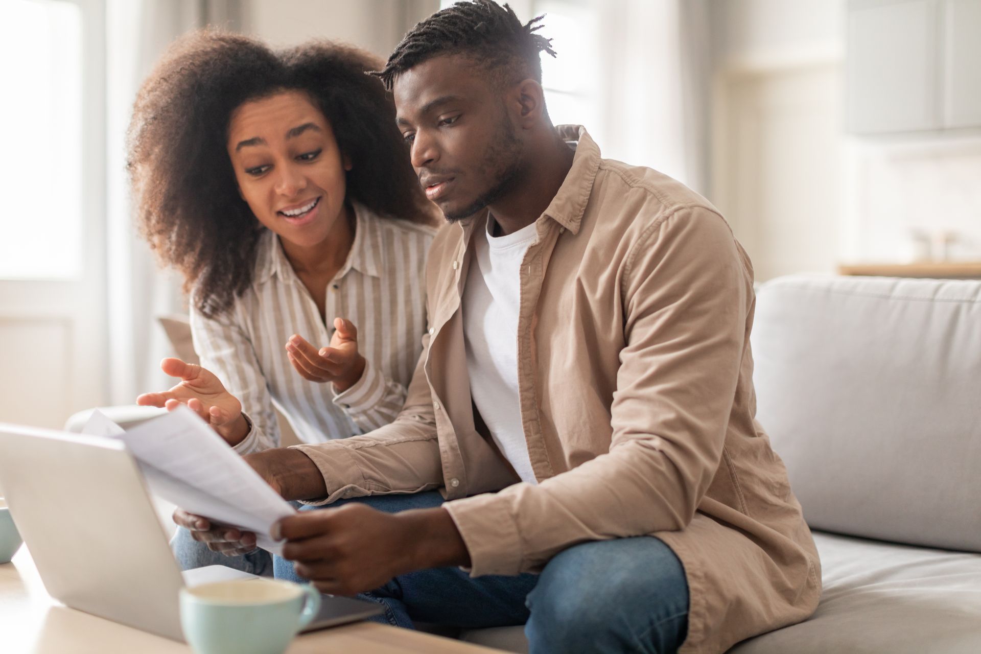 Two people reviewing papers and a laptop together on a couch in a bright living room