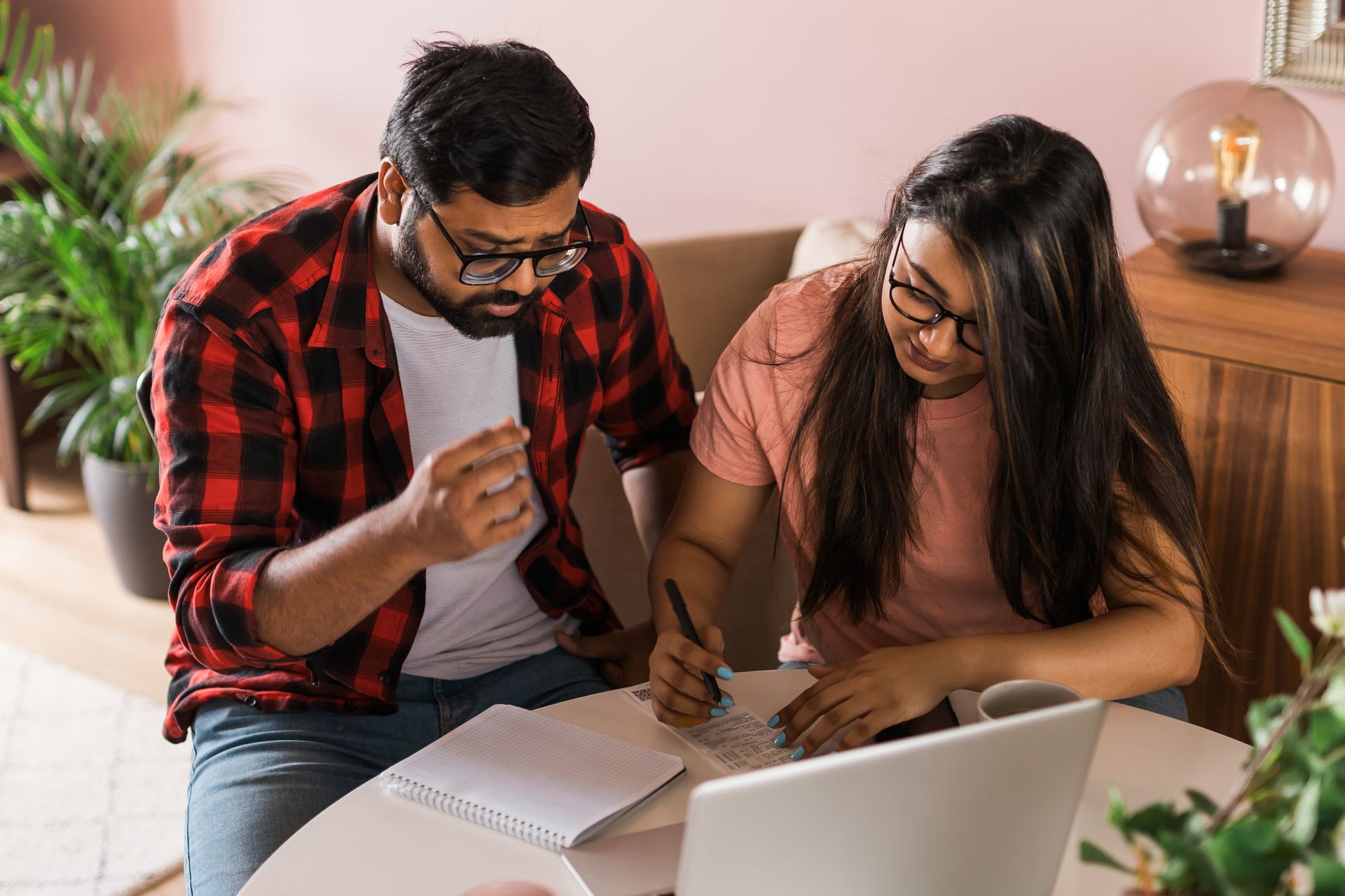 Two people reviewing papers together at a table with a laptop in a cozy room