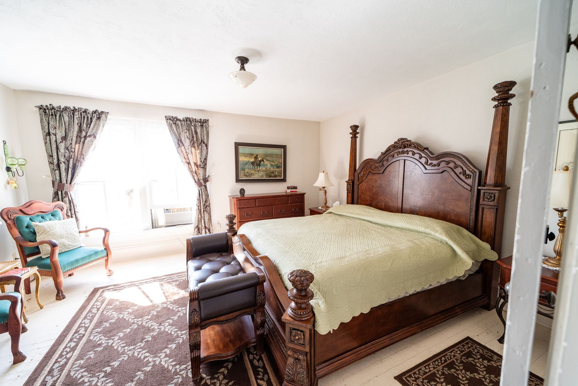 A bedroom featuring a large wooden four-poster bed with a green spread, a patterned rug, a chair, and a dresser.