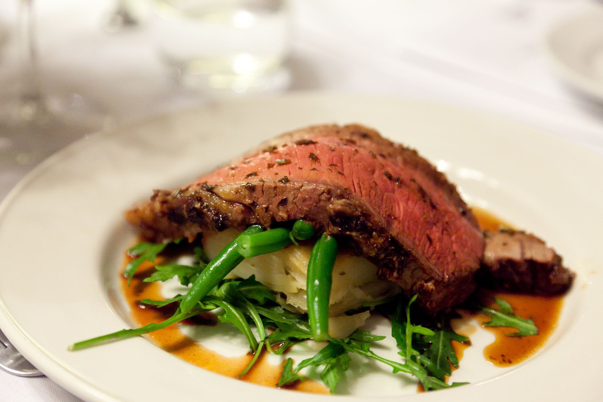 A sliced steak served over mashed potatoes and greens with sauce, plated on a white dish.