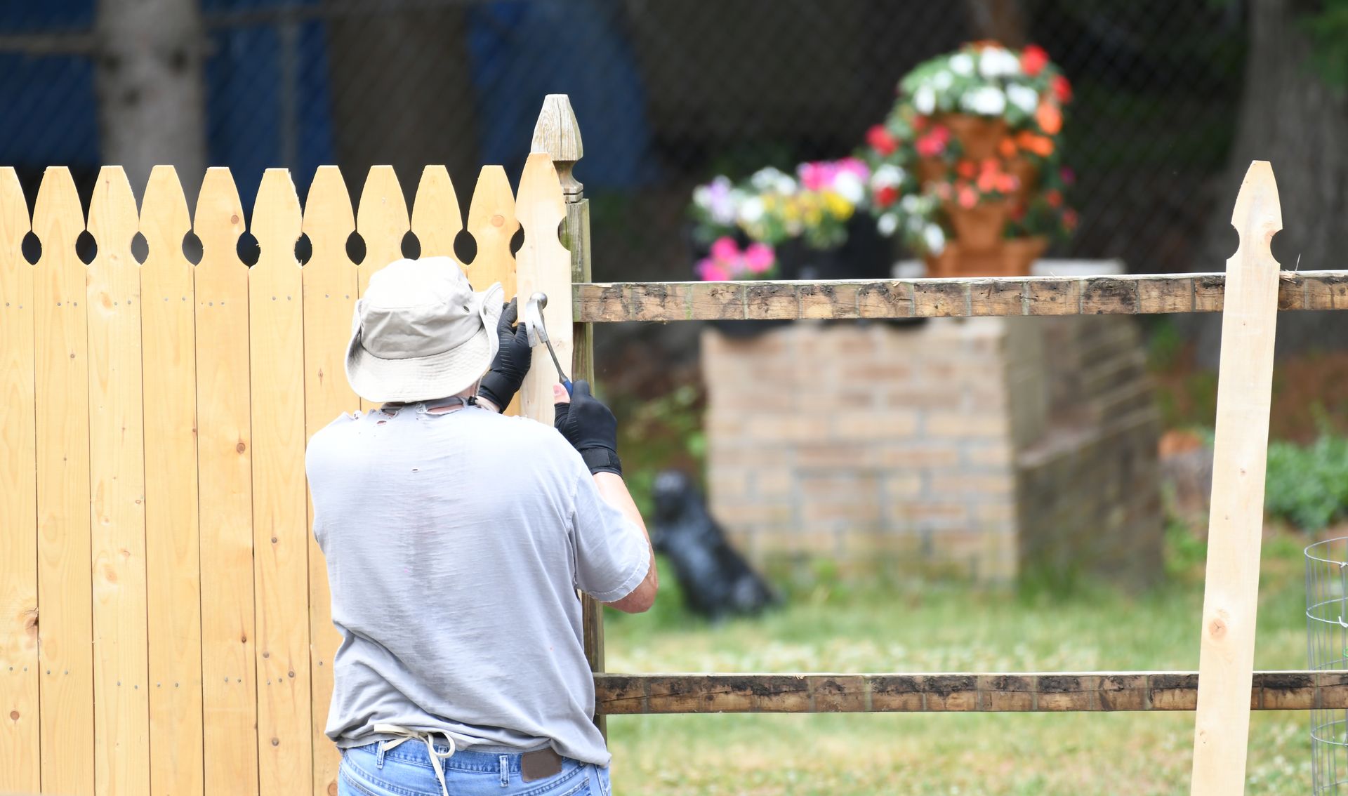 A man is fixing a wooden fence in a backyard.