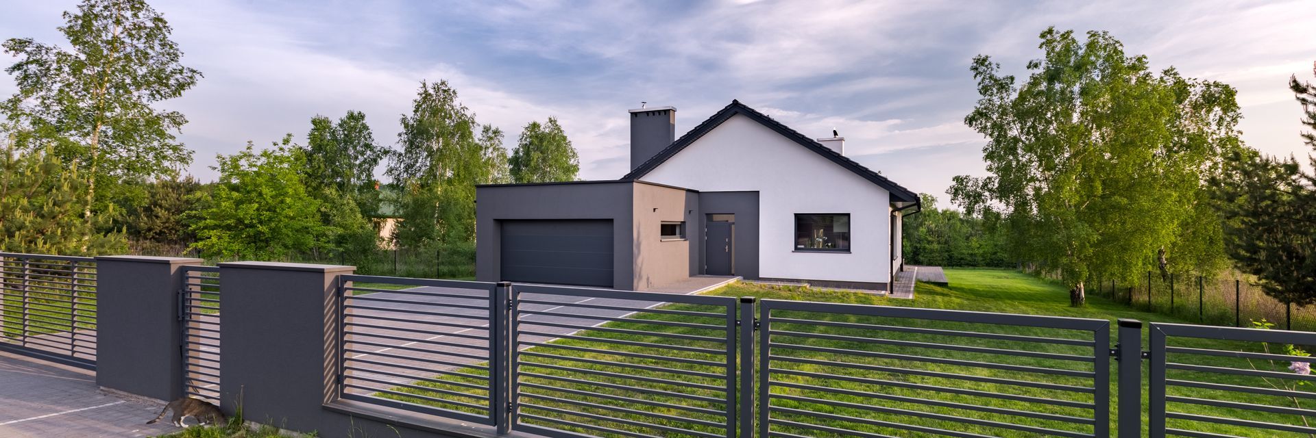 A modern white house with a black roof, gray garage, and fence in a green yard.