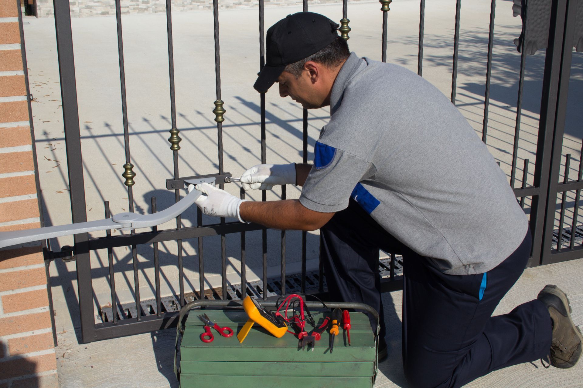 Man in uniform kneeling, repairing a gate opener with tools