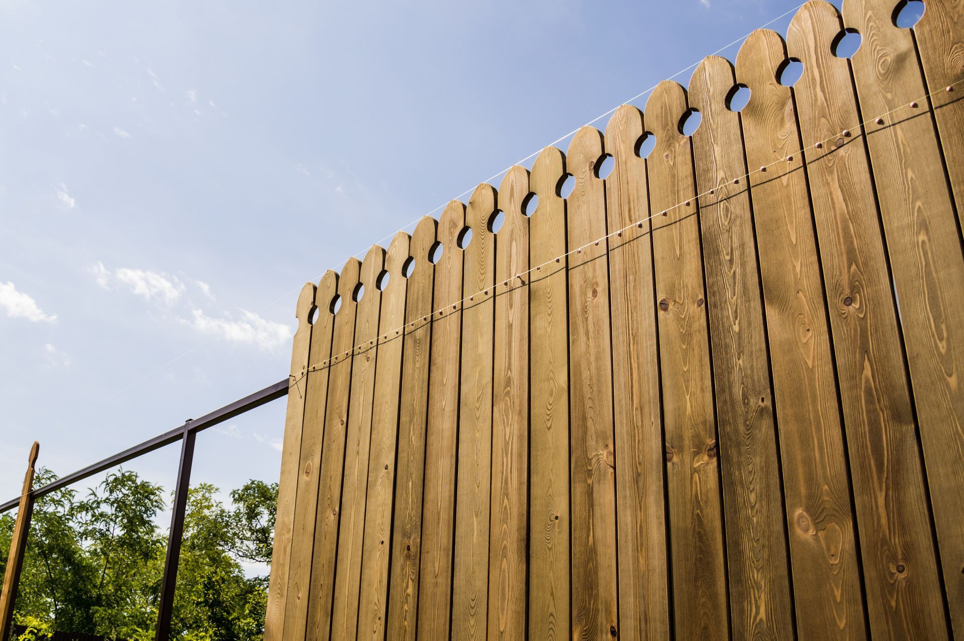 Wooden fence with decorative circular cutouts against a blue sky.