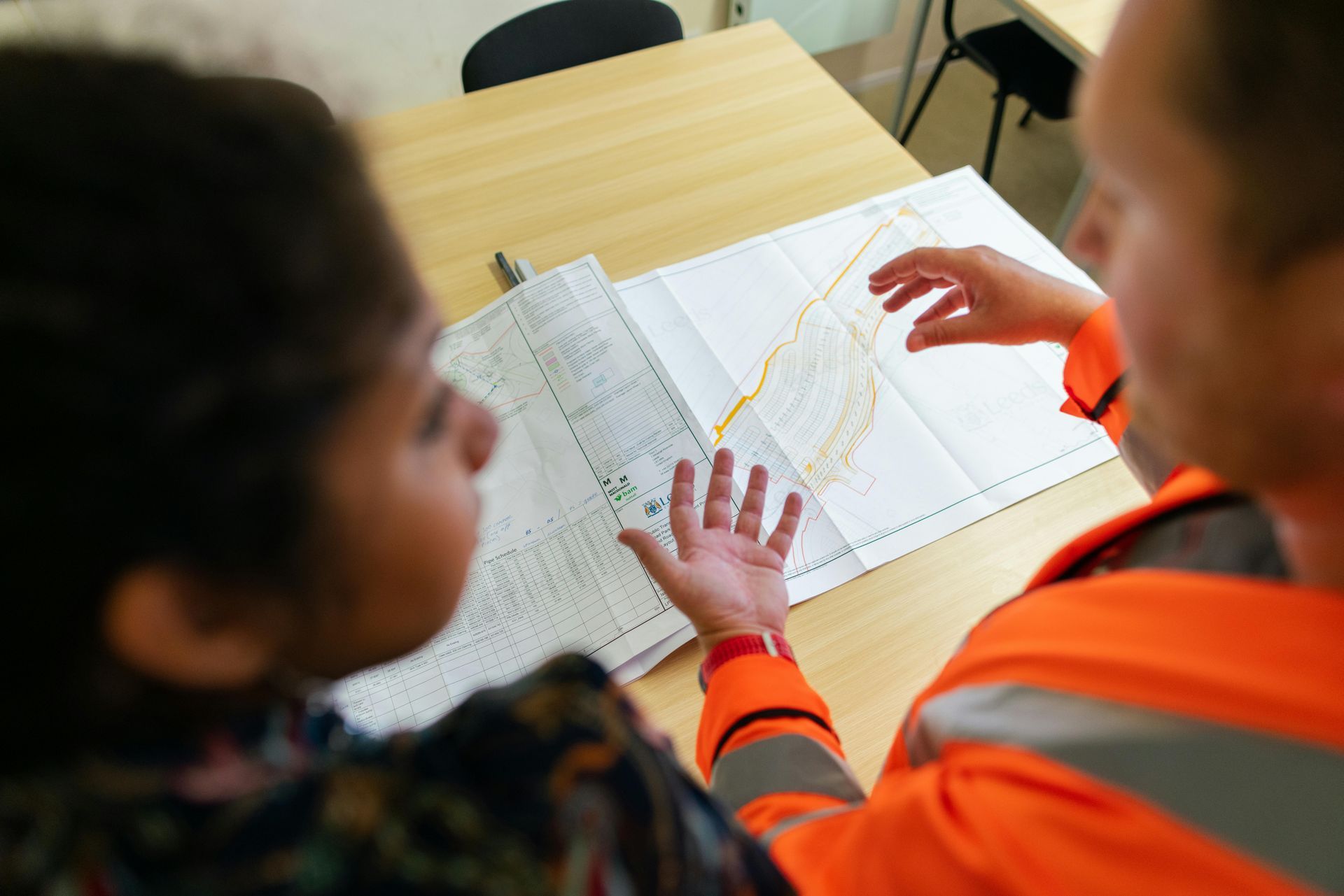 Two people looking at a map. One points, the other watches intently. Indoors, at a desk.