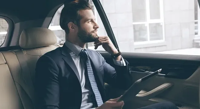 A man in a suit and tie is sitting in the back seat of a car.