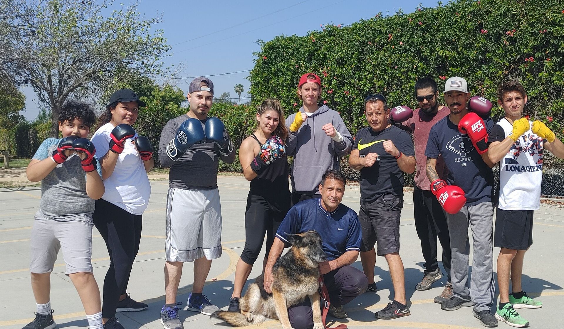 Group of people wearing boxing gloves posing outdoors; dog in front.