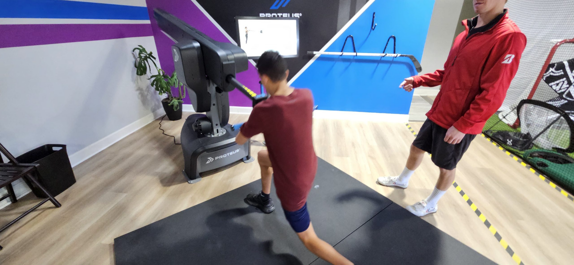 A man is stretching his legs in a gym while a man stands behind him.