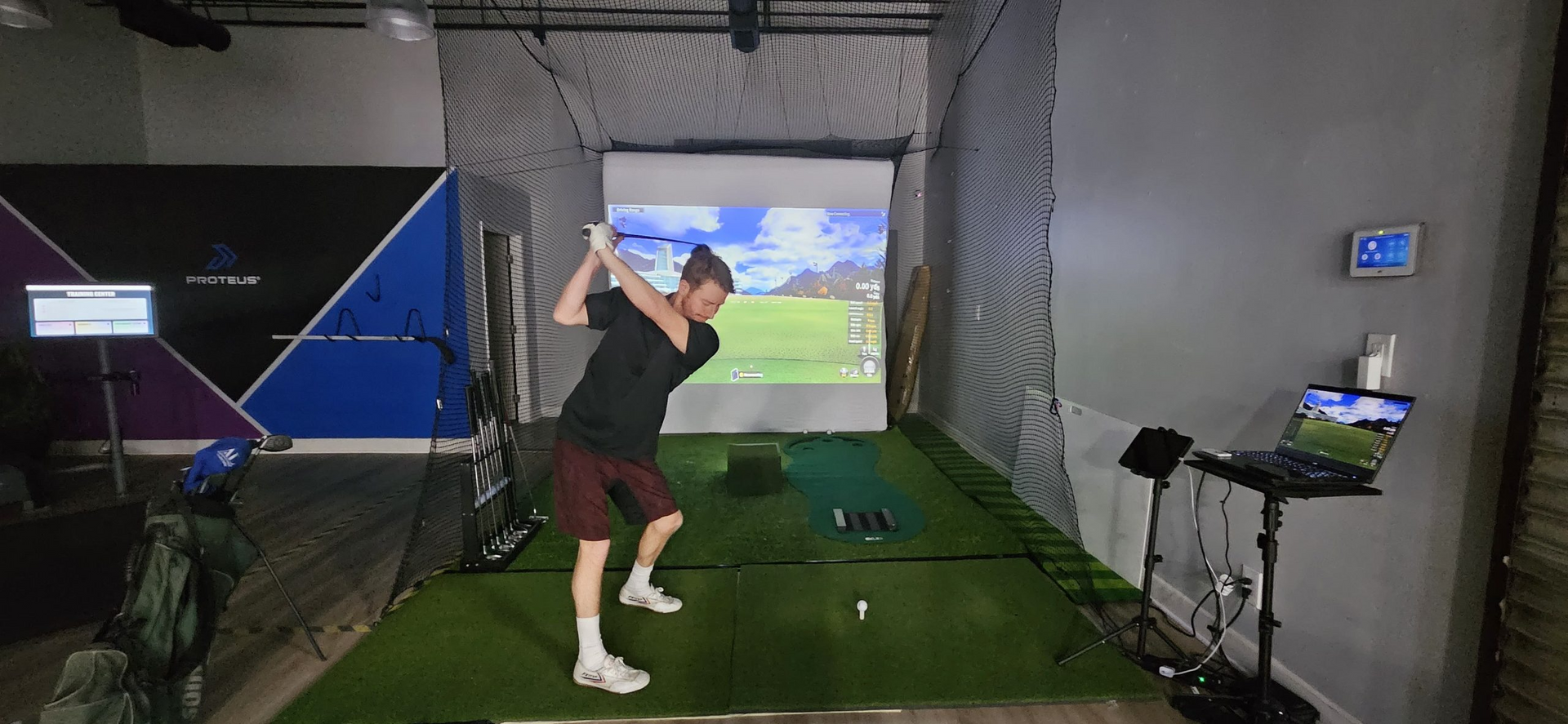 A man is swinging a golf club in a golf simulator.