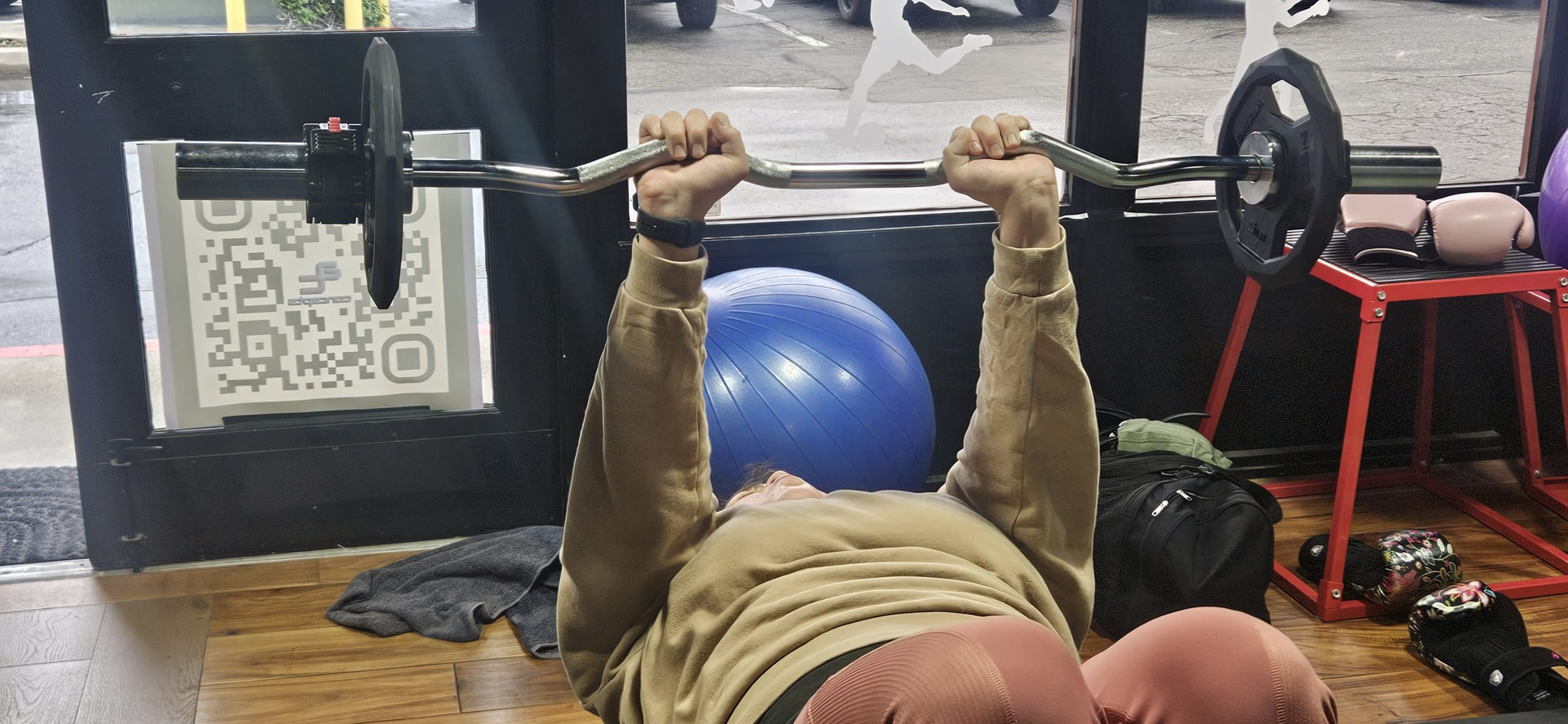 A man is laying on the floor lifting a barbell in a gym.