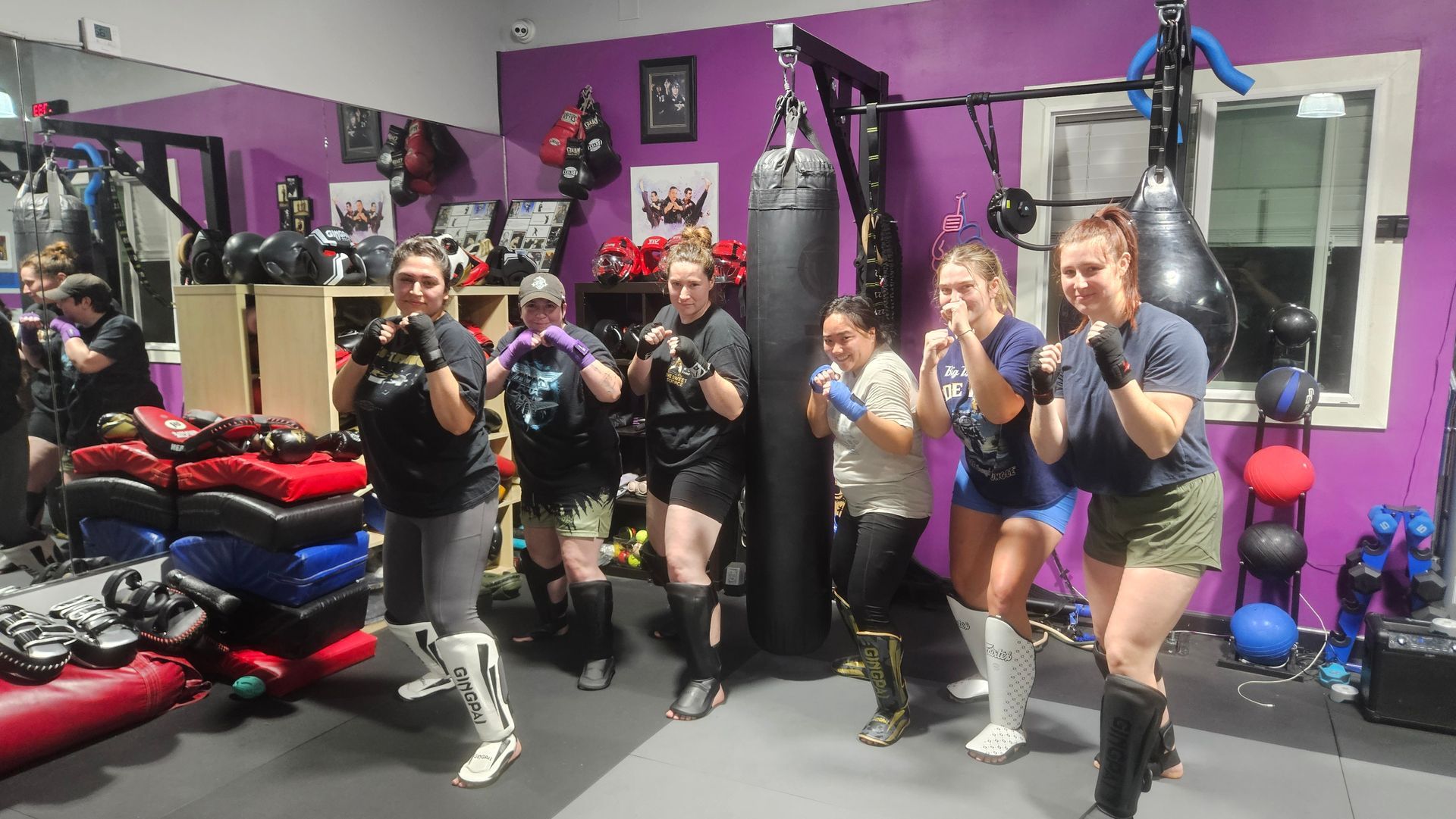 Group posing with boxing gloves in a purple gym beside a hanging heavy bag