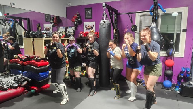 Group posing with boxing gloves in a purple gym beside a hanging heavy bag