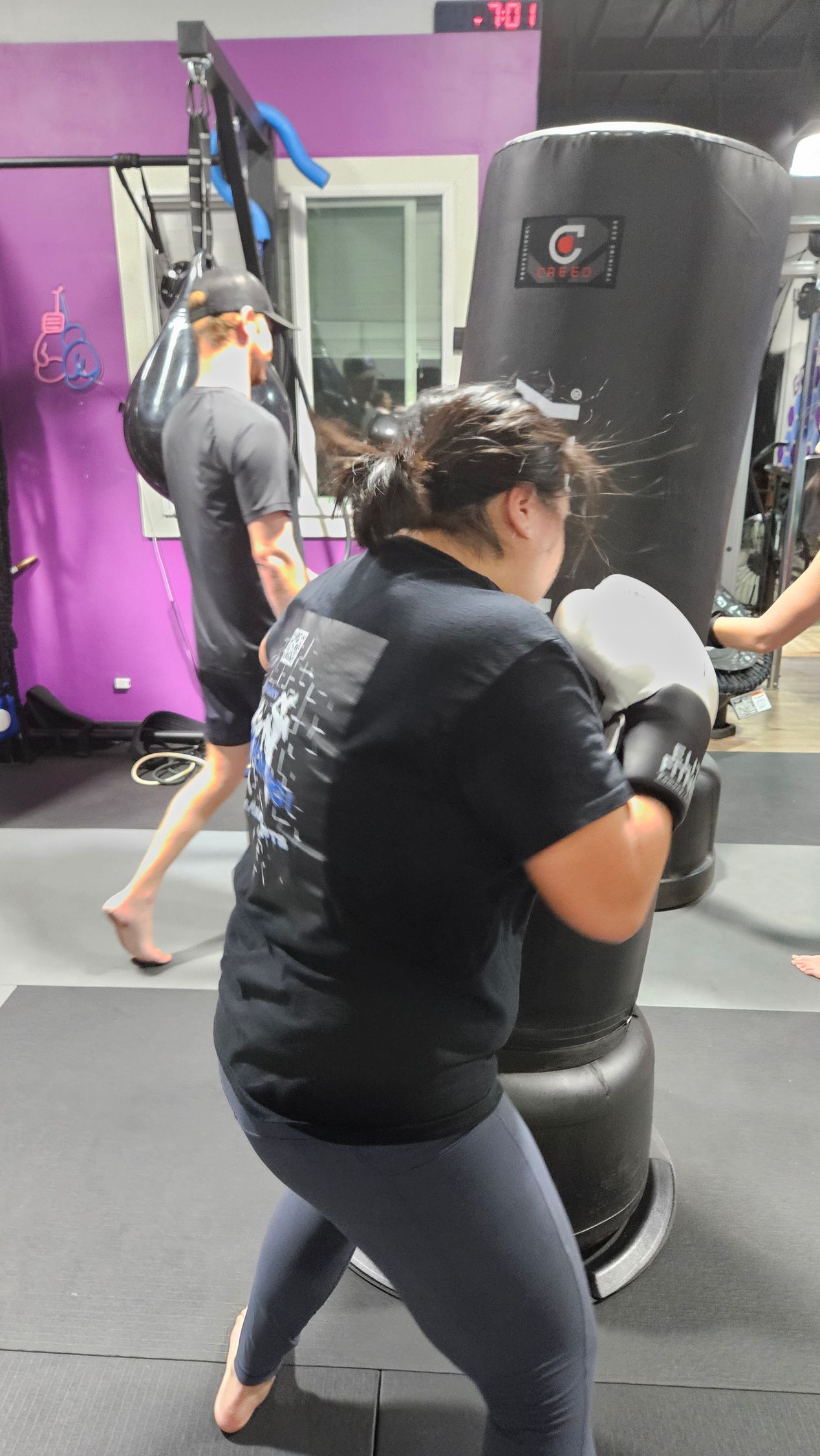 Woman boxing a black punching bag in a gym, wearing a black shirt and gray leggings.