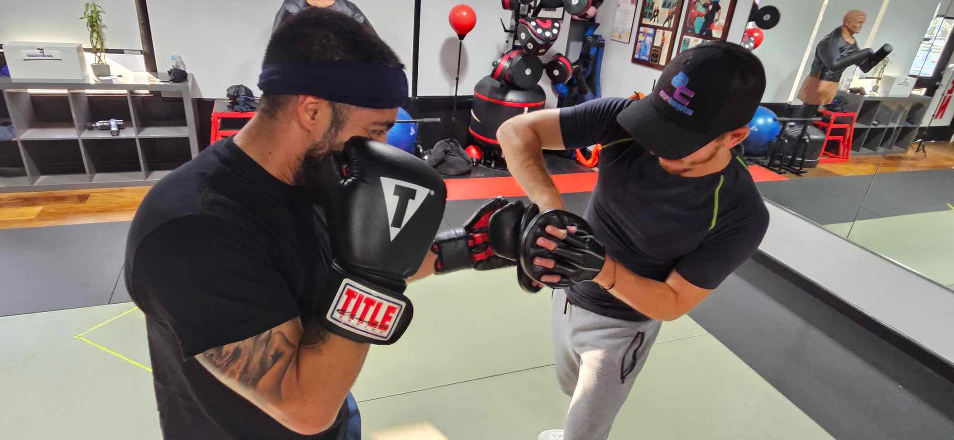 Two men wearing boxing gloves are standing next to each other in a gym.