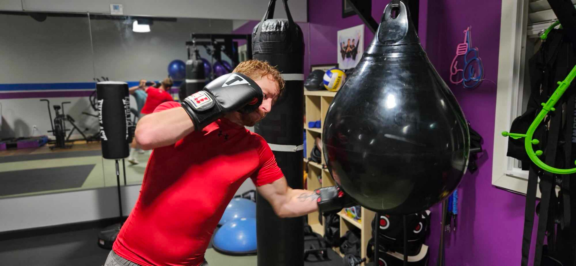 A person in a red shirt is boxing a hanging black bag in a gym.
