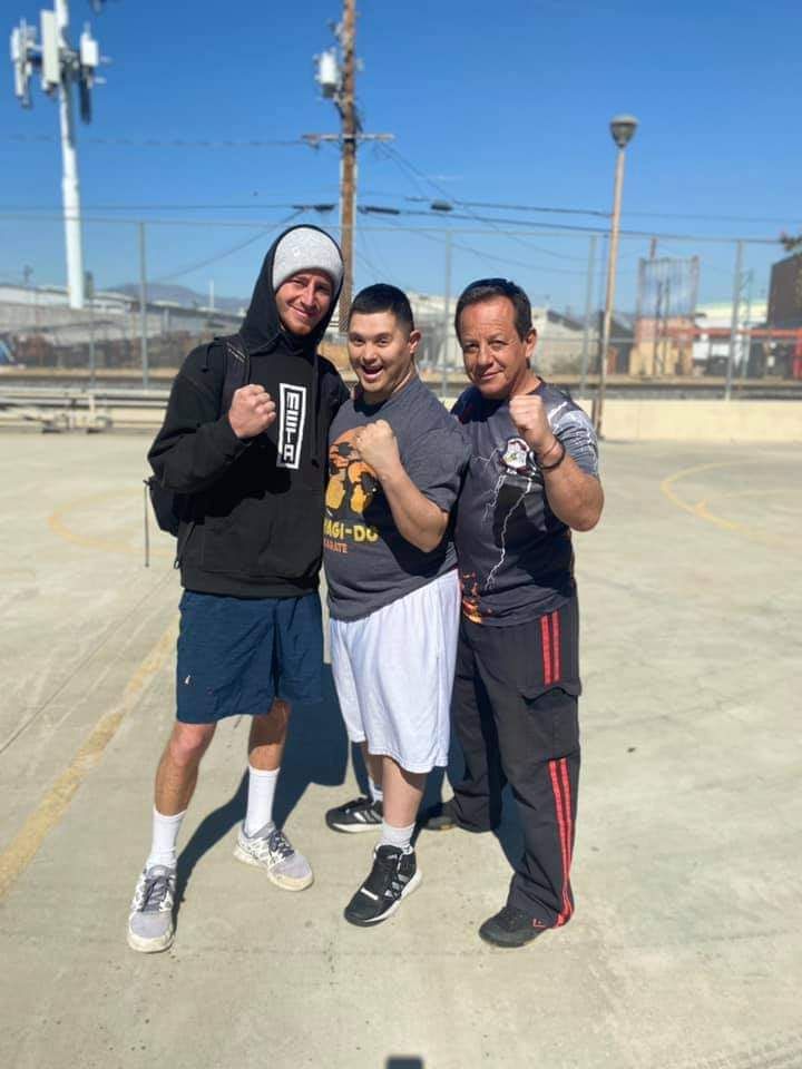 Three people posing, fists up. Outdoors, bright day. Two men on either side of one.