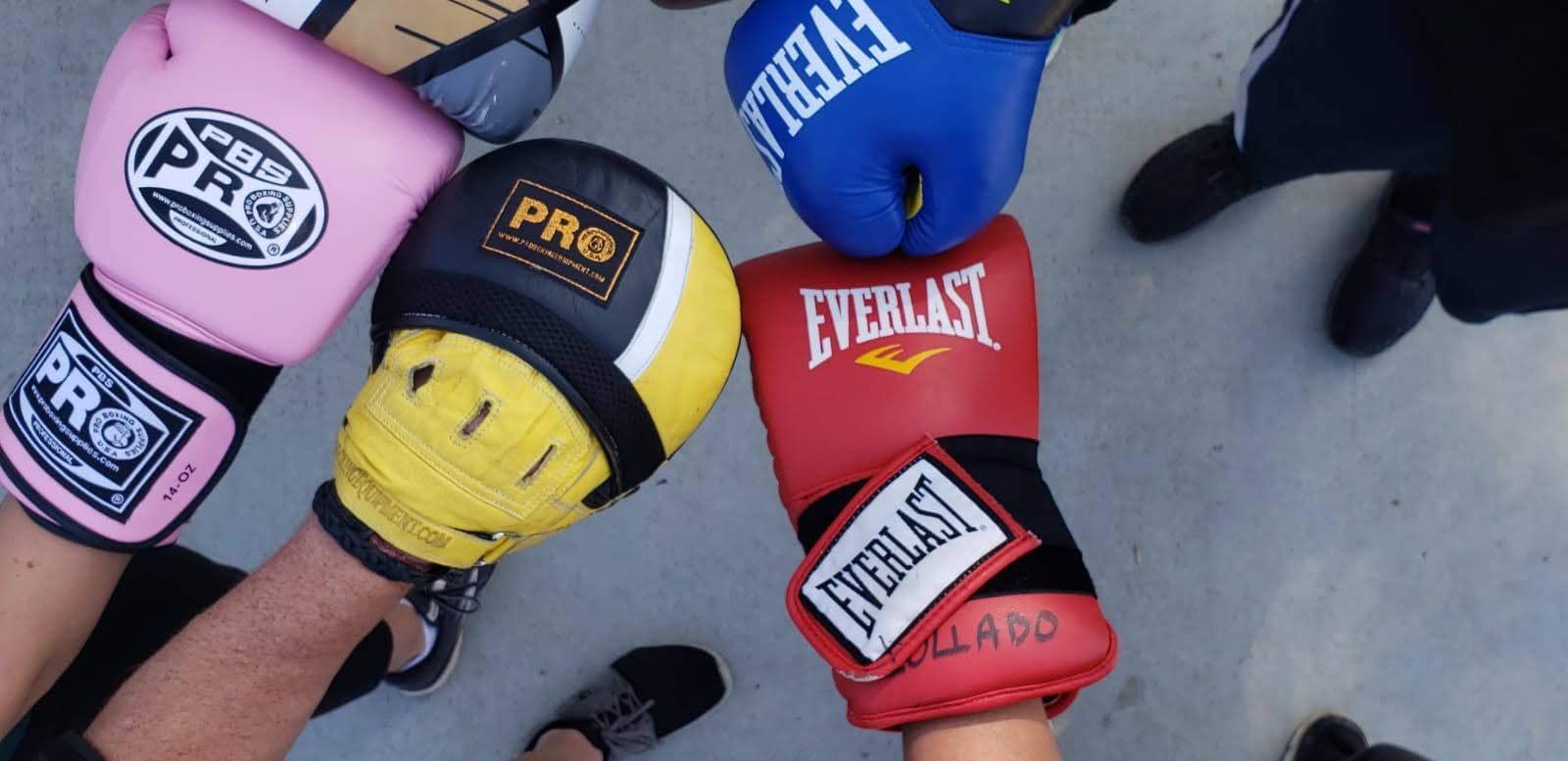 Hands wearing boxing gloves in pink, blue, red, and yellow, touching together.
