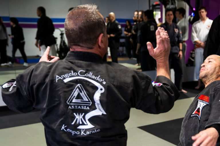 A man in a black karate uniform is standing in front of a group of people