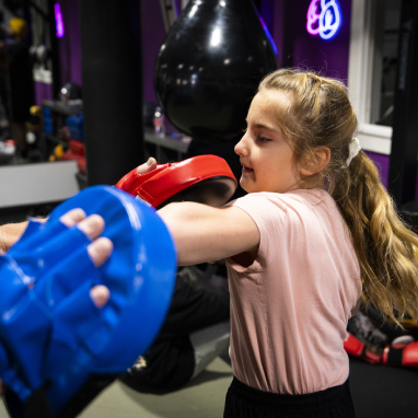 A young girl is wearing boxing gloves and a pink shirt