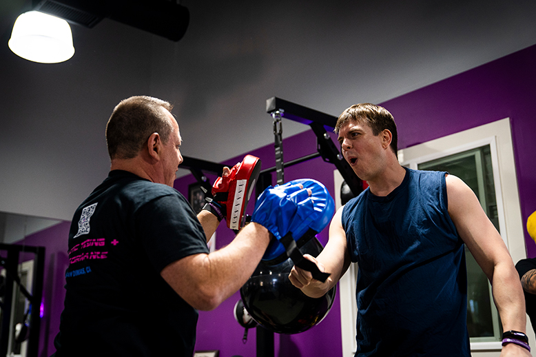 Man boxes with trainer in a gym. Trainer holds pads. Purple wall.