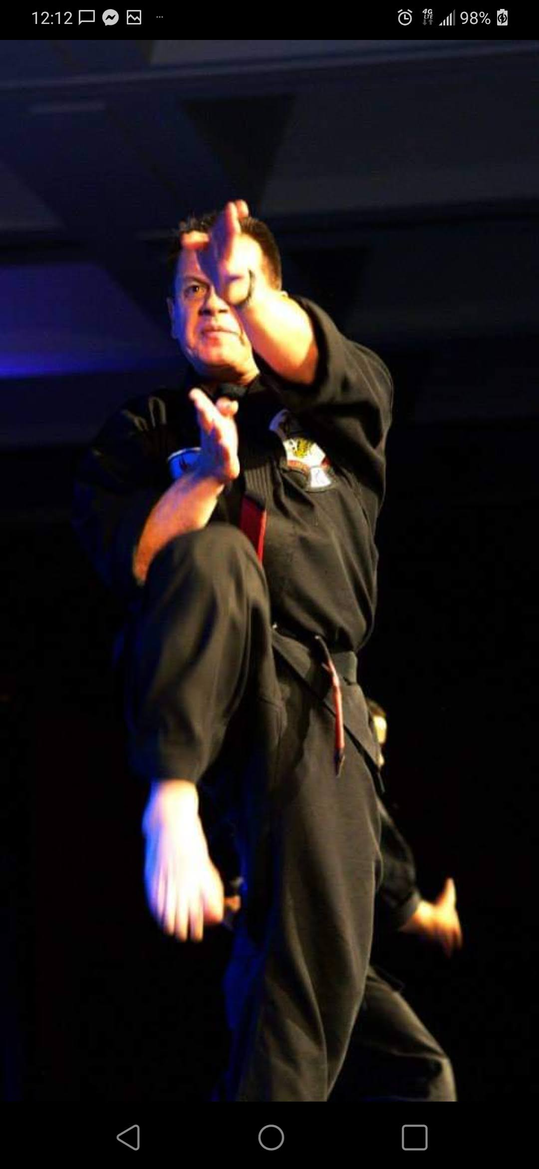 A man in a black karate uniform is kicking in the air.