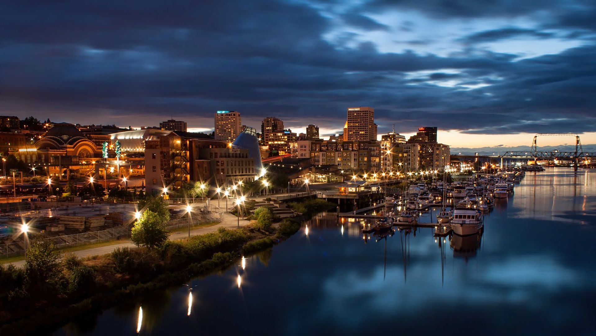 Night view of downtown Tacoma waterfront skyline with city lights reflecting on the water.