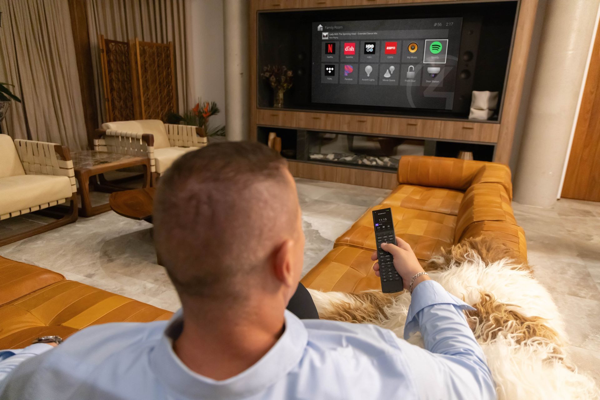 Person on a brown leather couch holding a remote, watching a TV in a wooden entertainment center.