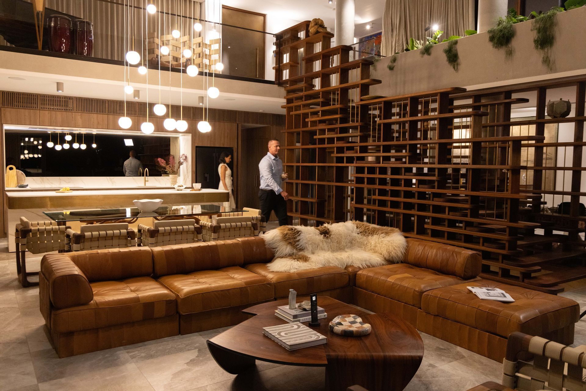 Living room with leather couches, wooden shelving, and a person walking.