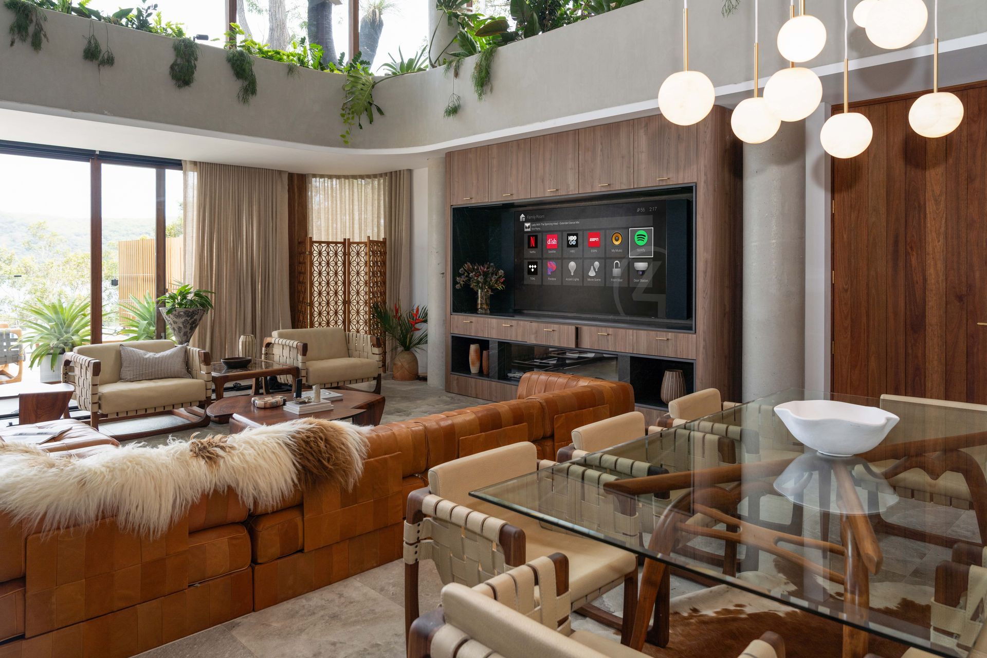 Luxurious living room with large TV, leather sofa, dining table, and green plants.