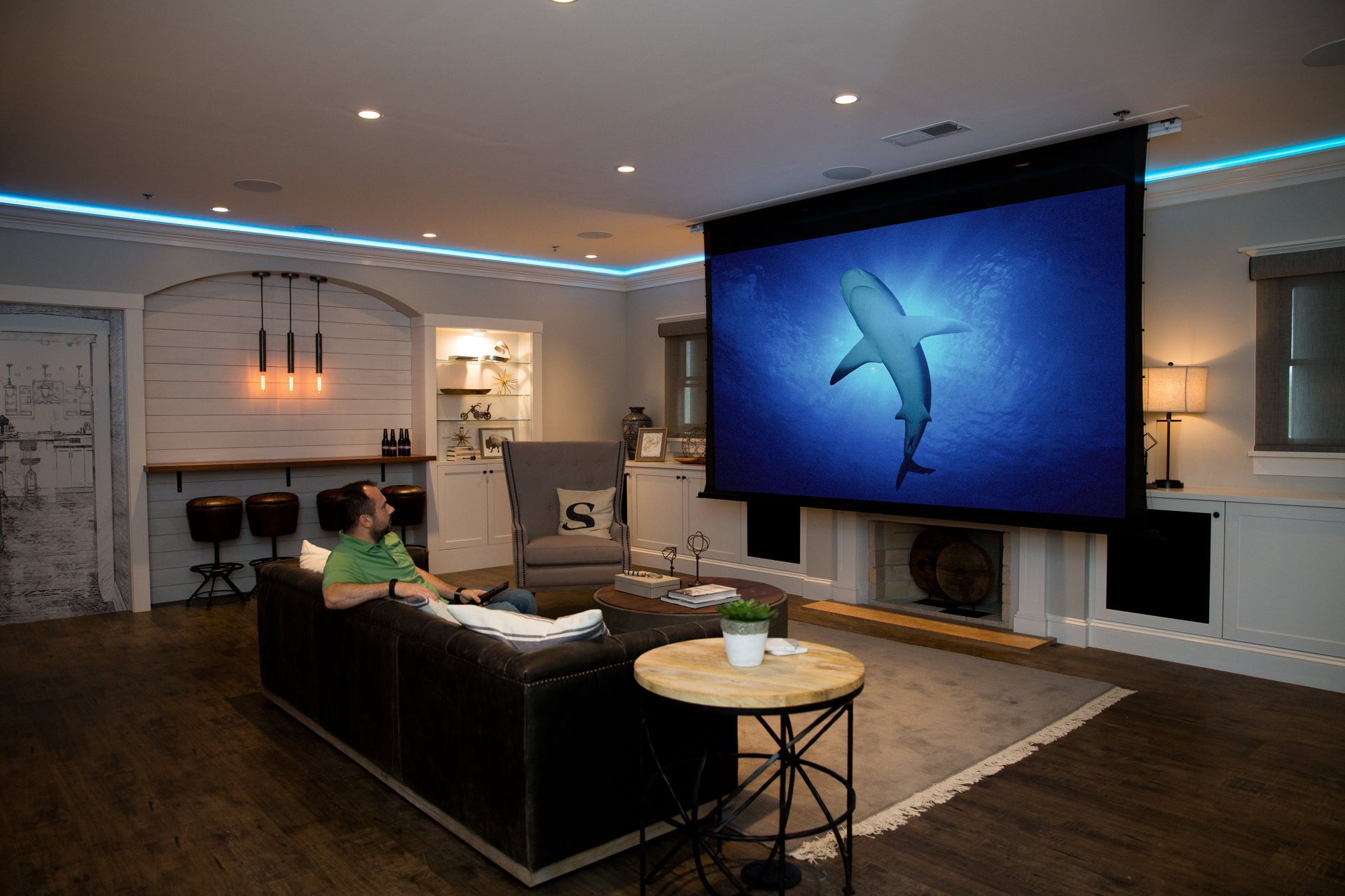 Man watches a shark movie on a large projector screen in a cozy home theater with dim lighting.
