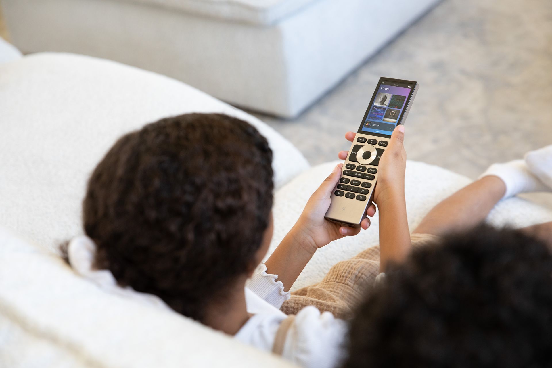 Person relaxing on a sofa using a Control4 Halo remote to manage smart home audio and entertainment, integrated by Rivas Technology Group.