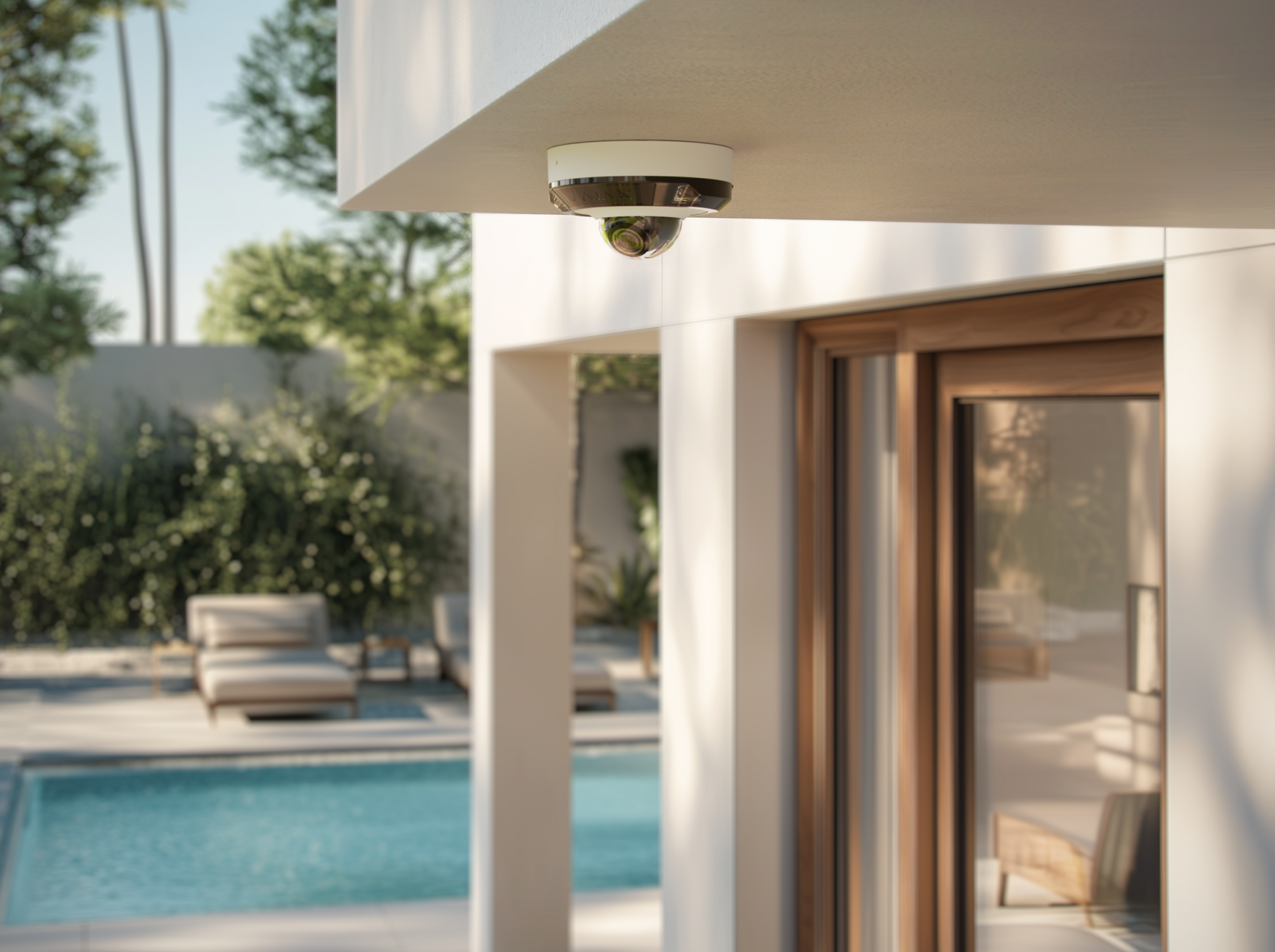 Security camera mounted on a white building's overhang, overlooking a pool and patio.