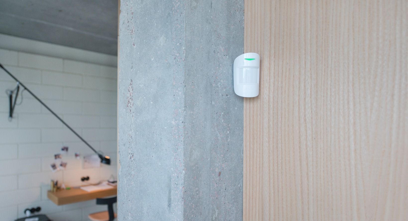 White motion sensor on a light wood panel near a concrete pillar in a modern interior.