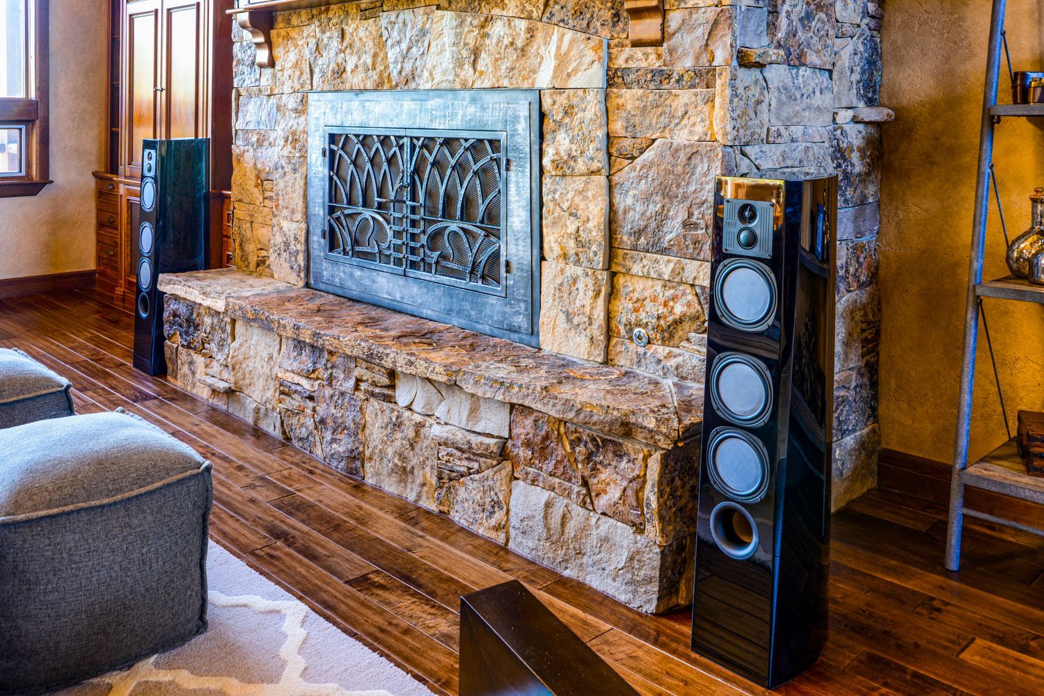 Two black speakers flank a stone fireplace in a living room with wooden floors.