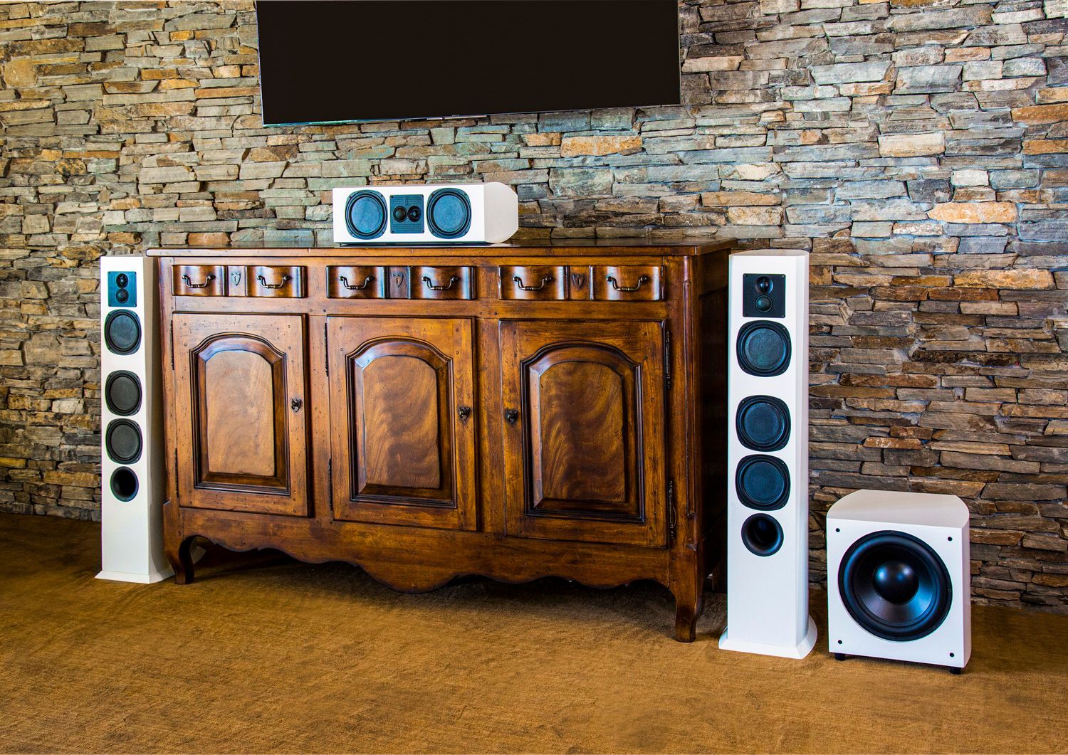 A home entertainment setup with a wooden cabinet, speakers, and a TV mounted on a stone wall.
